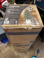 Boxed NOMA artificial Christmas tree packaging showing brand, model, and general item details.