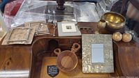 Wide view of assorted decorative items on wooden surface including pewter frames, mirror, wooden and metal bowls, candlesticks and small sculptures.