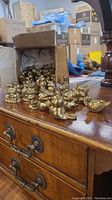 Cardboard box filled with many small brass animal figurines, mainly ducks and other bird shapes, placed on a wooden furniture surface.