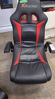 Front view of X Rocker gaming chair showing black and red faux leather seat with rip in middle.