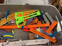 Large plastic bin filled with assorted Hot Wheels tracks and accessories in orange, yellow, green, blue, and gray colors.