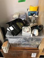 Overview of assorted household items in plastic container including Batman clock, timer, handheld vacuum, and hardware.