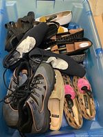 Multiple assorted pairs of ladies footwear inside a large blue plastic tote. Visible are black sandals, white flats, moccasin-style shoes, leopard print and pink flats, and sporty shoes.