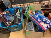 Photo of blue plastic bin containing LEGO Star Wars and Game of Thrones sets along with additional boxes including Tobbie robot and dinosaur puzzle, showing lot contents.