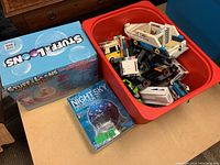 Overview photo showing red bin filled with assorted Lego vehicles and pieces, with Stuff-A-Loons and Night Sky Projection kits beside it.