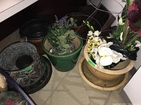 Photo showing several planters including a green ceramic pot with faux lavender and a beige plastic pot with faux flowers inside, plus a metal tomato cage.