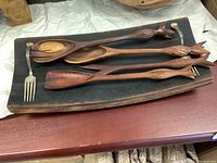 Five piece wooden salad set displayed on a light fabric surface with wooden salad tray and four utensils with pinecone carved handles.