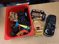 Red plastic bin filled with assorted toy vehicles and parts including black motorcycle, orange and blue vehicles.