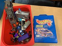 Photo of red container with various small toy vehicles and a blue Hot Wheels carrying case.