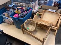 Overview of bins and items on table including dolls, plush toys in clear and blue plastic bins, wicker bassinet, and wooden toy furniture pieces