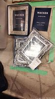 Three silver plated photo frames are shown. One frame is out of packaging, two remain in original packaging with Wacker branding. Frames fit 5x7 photos and have ornate decorative borders.