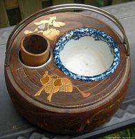 Top front angle showing carved bird and floral inlay on wood surface, enameled inner ceramic bowl with blue speckled rim, bamboo cup holder, and metal handle.