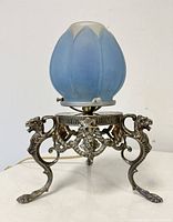 Front view of lamp unlit showing pastel blue lotus-bud art glass shade and silvered metal gryphon-footed base.