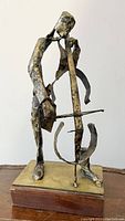Front view of abstract metal cello player sculpture on wooden base
