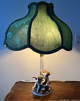 Front full view of porcelain cherub table lamp with green silk shade illuminated.