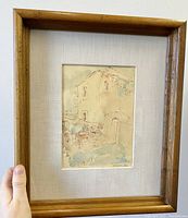 Full view of the maple wood framed watercolour painting depicting a rustic building scene in earth tones.