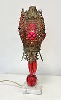 Front view of vintage ruby red boudoir lamp with detailed filigree metal overlay and faceted glass body on marble base.