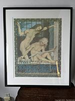 Photo of framed art poster hanging on wall, showing two nude figures and German text below.