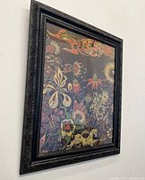 Angled view of the framed print on wall showing ornate black carved frame and visible floral and animal motifs