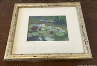 Framed pastel painting showing lilypads and water lilies, with a metallic distressed frame and matting visible.