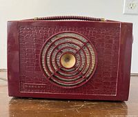 Front view of burgundy bakelite radio with embossed crocodile skin pattern and central speaker grille.