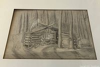 Front view of framed grayscale drawing of a log cabin in woods with a man stirring a pot and a horse at left; signed lower right.