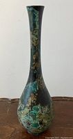 Front view of tall slender bronze vase on wooden surface showing green verdigris patina