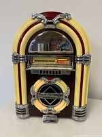 Front view of vintage Crossley table-top jukebox showing illuminated cream and maroon bands, chrome trim, and clear display for tuning and cassette mechanism.