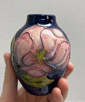 Front view of the small vase showing the prominent pink magnolia flower with green leaves on a dark blue glossy background.