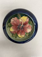 Top view of round trinket dish showing detailed vibrant hibiscus flower in red and yellow with green leaves and a blue rim.
