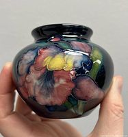 Front view of small William Moorcroft vase showing pink and yellow iris flowers raised on deep blue base.