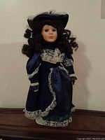 Front view of porcelain collectible doll in blue Victorian dress with lace.