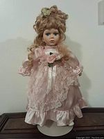 Front view of collectible porcelain doll in pink satin and lace dress, showing facial features and dress details