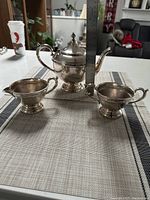 Front angle of three-piece silver plated tea set featuring teapot, creamer, and sugar bowl on a cloth.