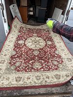 Full view of the red and beige floral patterned area rug being held up showing design and colors.