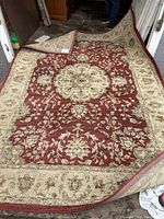 Full view of the red and beige floral patterned carpet showing its design and condition.