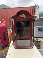 Front view of a dark wooden display box with glass door and decorative top showing a carved shell motif.