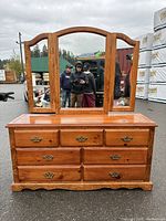 Front view of wooden dresser showing seven drawers and three-panel mirror with arched tops.