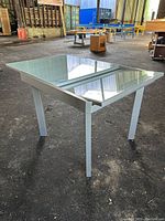 Glass top expandable dining table with metal legs, side view showing expanded width.