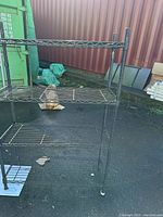 Front angle view of black metal frame roller shelf with four wire mesh shelves outdoors on asphalt.
