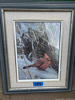 Framed picture showing a red cardinal bird on snow with tree branches and bark in the background