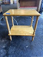 Front view of the pine shelf showing two flat shelves and turned legs on a rough black surface