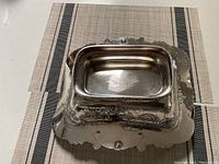 Top view of sterling silver rectangular basket with ornate floral and scroll detailing on edges and sides.