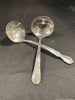 Two silver serving spoons with visible handle patterns on a black background