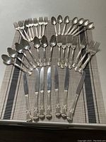 Full set of silver plate cutlery displayed on a cloth with 7 knives, 7 forks, 7 spoons laid out.