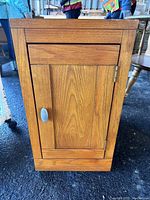 Front view of the oak slide out shelf unit showing the paneled door with silver handle.