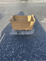 Front side view of a rectangular wicker basket with wooden handles, sitting on pavement surface showing dimensions visually.