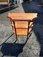 Three-quarter view of the wood shelf showing all three tiers and turned legs on an outdoor surface with shadows.