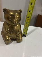 Front view of brass bear coin bank with measuring tape showing approximately 5.5 inches height.