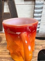 Close-up of one Fire King mug showing red to orange color gradient and textured diamond pattern with handle